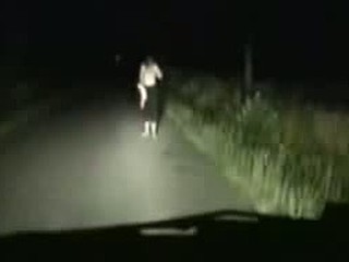 A movie scene of a girl stripping infront of a car for a ride. She is shown off by the headlights and it furns out to be a great time for both her and the guy driving